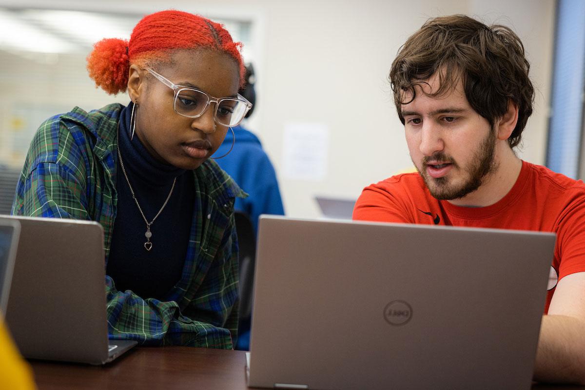 Two students both focusing on a laptop having a conversation